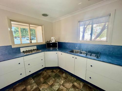 达博West View Caravanpark的厨房配有白色橱柜、水槽和2扇窗户。