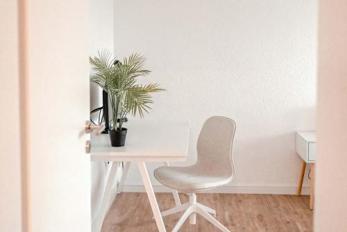 诺伊斯Apartment mit Küche, Arbeitsplatz und XXL Sofa的一张带椅子和植物的白色书桌