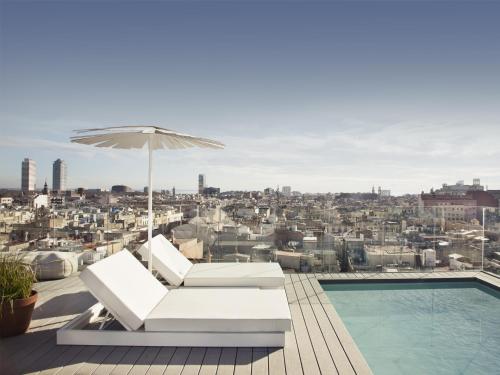 巴塞罗那尤尔板特拉法加酒店的一个带游泳池、遮阳伞、椅子和游泳池的庭院