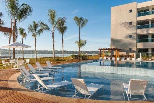 巴西利亚Luxuoso Flat Brisas do Lago Terraço Aconchegante的一个带白色椅子的游泳池、一座建筑和棕榈树