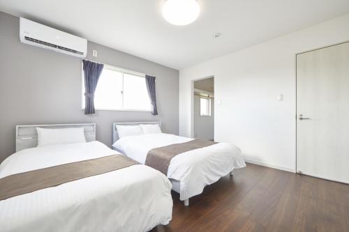 濑底villa PILINA的配有白色墙壁和木地板的客房内的两张床