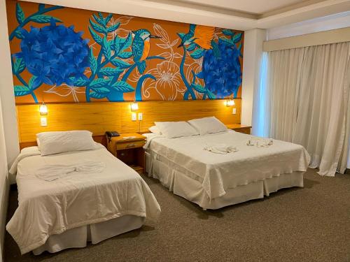 CapiatáLos Lagos Resort Hotel的酒店客房设有两张床,墙上挂有绘画作品