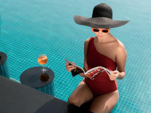 迪拜Sofitel Dubai The Obelisk的坐在游泳池中的穿着泳衣和帽子的女人