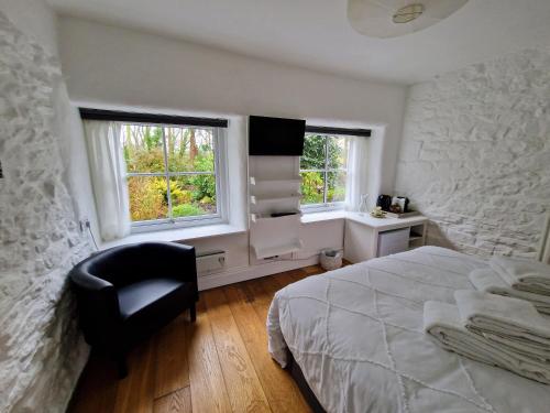 赫尔斯顿Primrose Cottage的一间卧室配有一张床和一把椅子,还有两个窗户