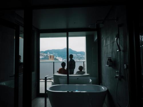 长崎FAV LUX Nagasaki的带浴缸的浴室以及2人眺望窗外
