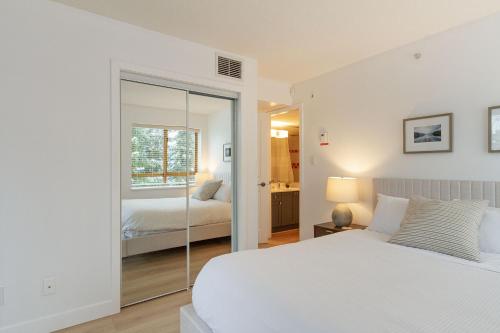 惠斯勒900 SQFT 2 Bed 2 Bath Renovated Suite at Cascade Lodge in Whistler Village Sleeps 6的白色卧室配有床和镜子