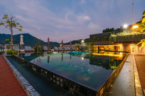 芭东海滩Rak Elegant Hotel Patong - SHA Extra Plus的一座晚上拥有山脉背景的游泳池