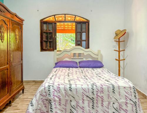 若阿诺波利斯Chacara com lazer e conforto em Joanopolis SP的一间卧室配有一张带紫色枕头的床和窗户。