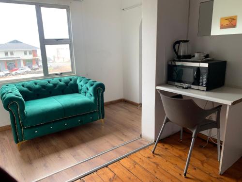 东伦敦Beach View B&B的一张绿色沙发,位于一个配有书桌和电视的房间