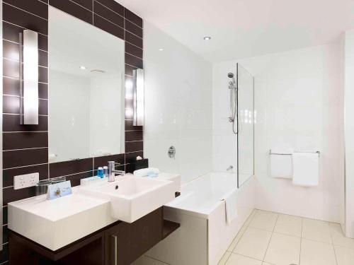 布里斯班布里斯班机场诺富特酒店的白色的浴室设有水槽和淋浴。