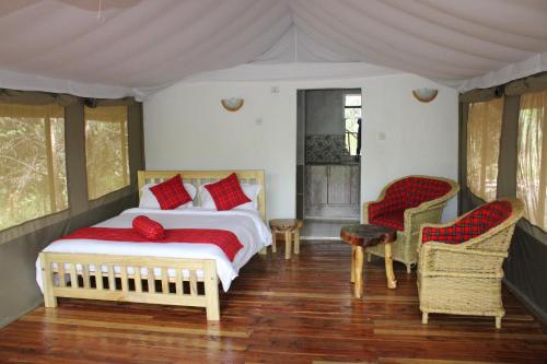 OlolaimutiekMara Empiris Safari Camp的一间卧室配有一张带红色枕头的床和两把椅子