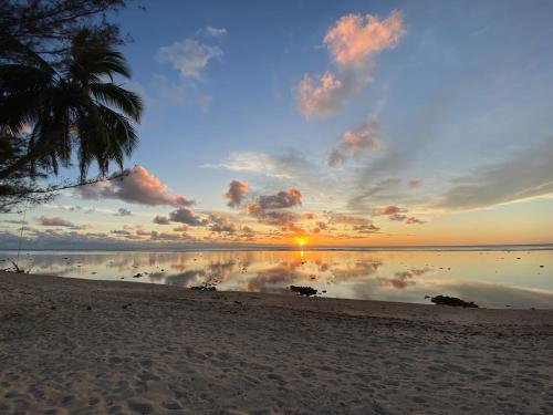 阿罗朗吉Te Moana Nui Villas的棕榈树海滩上的日落