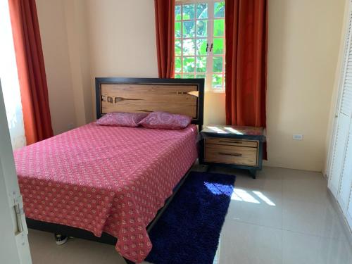 西班牙港Quiet 2-bed property within the centre of city的一间卧室配有一张带红色床罩的床和窗户