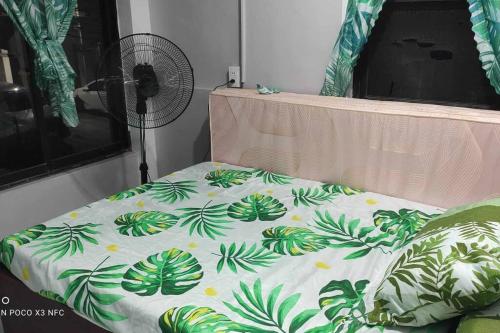 奥隆阿波Baloy beach house的一张带绿色和白色棉被的床和一个风扇