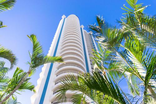黄金海岸Aegean Resort Apartments的一座高大的建筑,前面有棕榈树