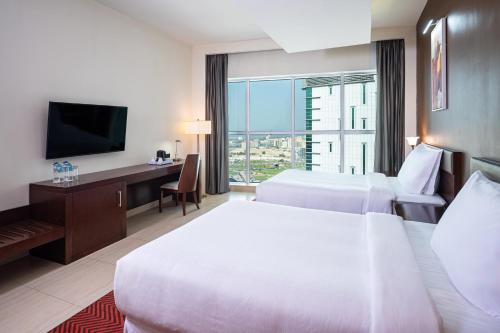 沙迦Four Points by Sheraton Sharjah的酒店客房设有两张床、一张桌子和一台电视。
