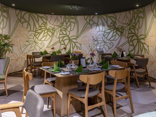 内罗毕Mercure Nairobi Upper Hill的墙上设有桌椅和植物的餐厅