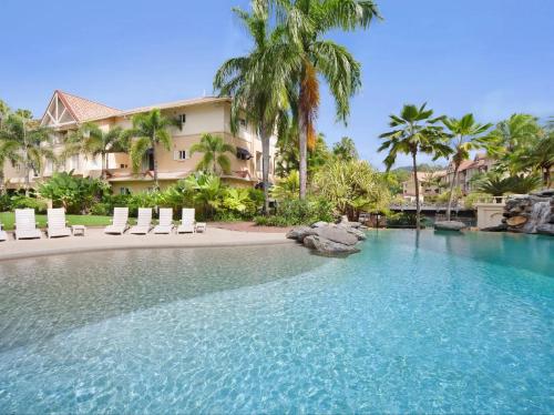Cairns NorthLuxury tropical 2bedroom apartment in resort 4 swimming pools的一个带椅子和棕榈树的度假游泳池