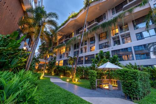 普吉镇HOMA Phuket Town的公寓大楼设有遮阳伞和花园