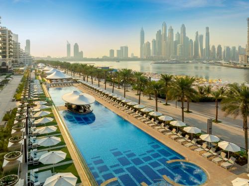 迪拜Marriott Resort Palm Jumeirah, Dubai的一座带遮阳伞和棕榈树的游泳池以及一个城市
