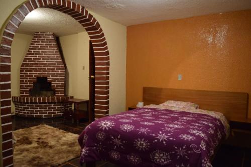 帕帕亚克塔La Quiteñita Papallacta的一间卧室配有紫色的床和砖墙