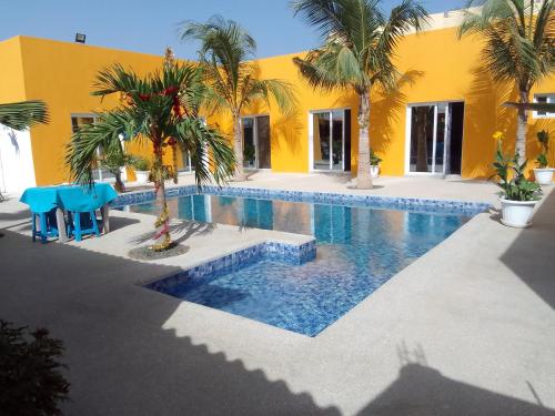 尼亚加Hôtel Colibri的一座棕榈树游泳池和一座黄色的建筑