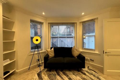 伦敦Chic Studio Flat 8 Mins to Harrods Knightsbridge的客厅配有黑色沙发和2扇窗户