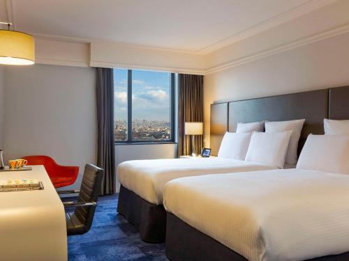 巴黎Pullman Paris Montparnasse的酒店客房,设有两张床和一张红色椅子