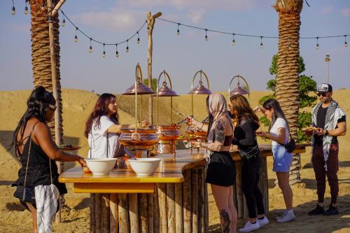 迪拜Al Marmoom Oasis “Luxury Camping & Bedouin Experience”的一群人站在桌子旁吃着食物