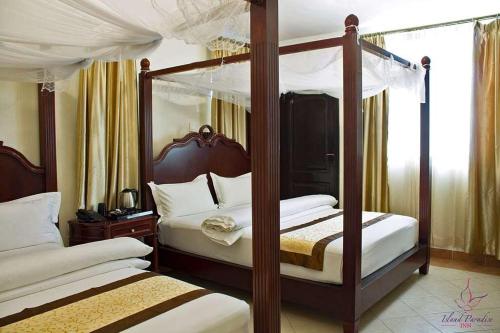 NgamboIsland Paradise Inn的一间卧室设有两张带白色床单的天蓬床。