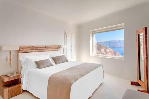 伊亚圣托里尼神秘豪华酒店的白色的卧室设有一张大床和一个窗户