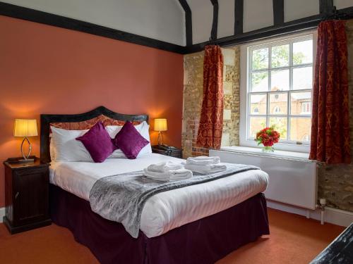 希钦Hitchin Priory Hotel的一间卧室配有一张带紫色枕头的大床