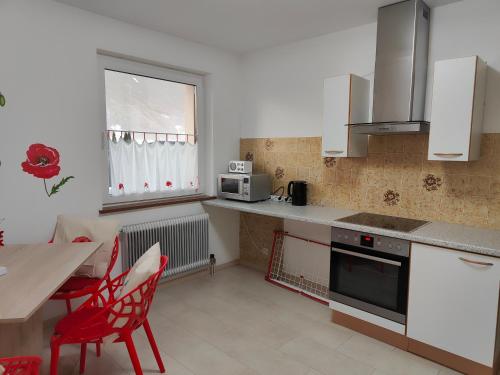 斯皮特安德劳Pension Hexagon的厨房配有白色橱柜、桌子和红色椅子