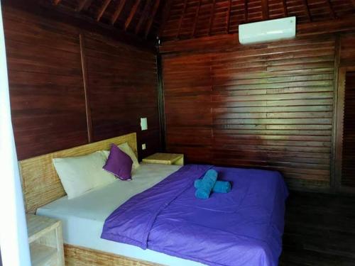蓝梦岛Bunutbali Villas88的木制客房内的一张床位,配有紫色床单和枕头
