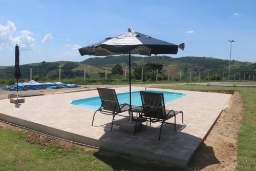 彼达迪Sítio Terra Sertaneja - Chalé Um Sonhador的游泳池前的两把椅子和一把遮阳伞