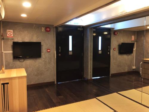 香港Espace Elastique B&B with contactless check-in的走廊设有两个黑色门和平面电视