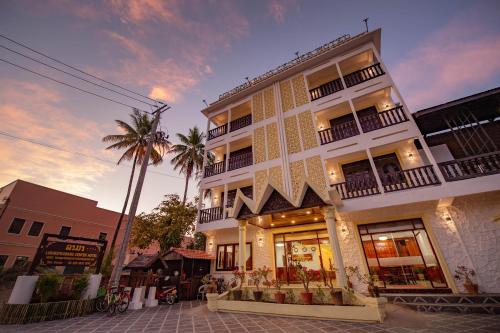 琅勃拉邦LuangPrabang Center Hotel的一座白色的建筑,前面有棕榈树