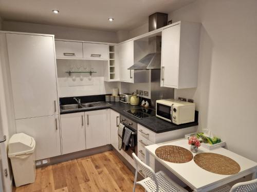 谢菲尔德Luxury Modern Apartment Stay的厨房配有白色橱柜、桌子和微波炉