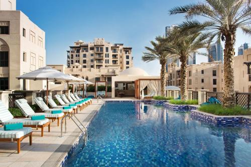 迪拜The Heritage Hotel, Autograph Collection的一个带椅子和棕榈树的游泳池,以及建筑