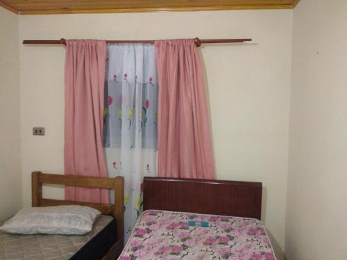 Guangualícasa familiar的一间卧室配有床和一个带粉红色窗帘的窗户。