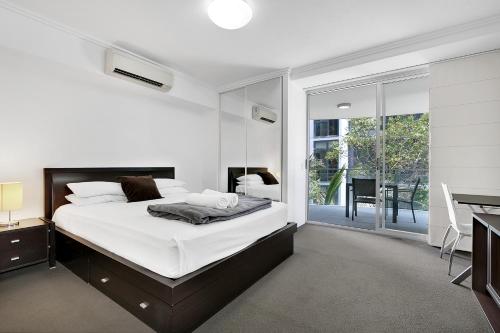 布里斯班South bank Serviced Apartments的白色的卧室设有床、书桌和窗户