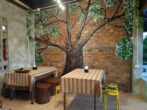 ต้นโพธิ์โฮมสเตย์的砖墙上有两个桌子和一棵树壁画
