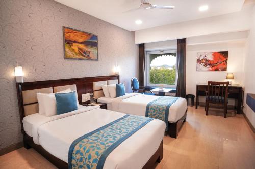 乌代浦地平线酒店的酒店客房带两张床和一张桌子以及椅子。