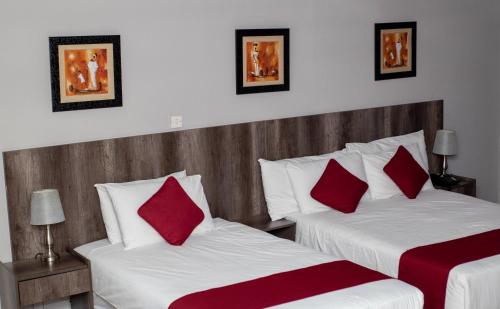 哈博罗内Platinum Hotel的一间卧室配有两张带红色枕头的床