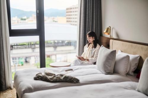 京都The Royal Park Canvas - Kyoto Nijo的坐在床上看着窗外的女人