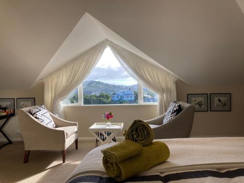 惠灵顿Khandallah Harbour View BnB的一间卧室配有一张床和两把椅子,并设有一个大窗户