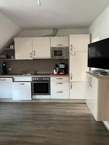 诺德奈Haus Julianne, Wohnung Backbord, Familie Poppinga的厨房配有白色橱柜和平面电视。