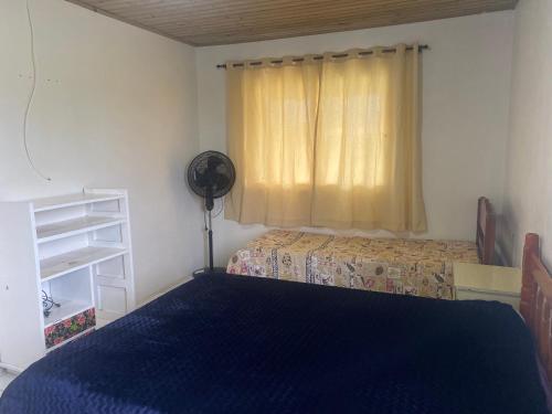 帕苏迪托雷斯Casa Praia Ribeiro SC的一间卧室配有一张床和一个带风扇的窗户。