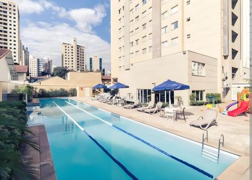 圣保罗M-Flat II Hotel - Vila Olimpia的大楼内带椅子和遮阳伞的大型游泳池