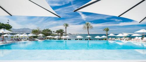 马斯喀特马斯喀特皇冠假日酒店的一个带白色遮阳伞和大海的大型游泳池